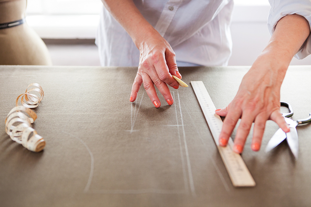 Close up. hands woman Tailor working cutting a roll of fabric on which she has marked out the pattern of the garment she is making with tailors chalk.